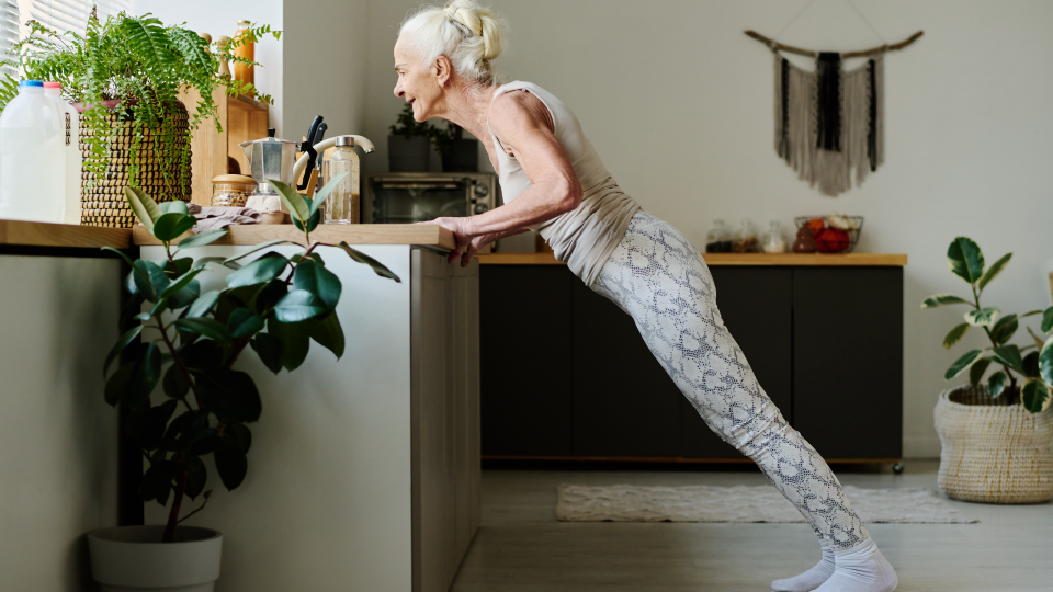 A woman does a push up leaning against her kitchen worktop